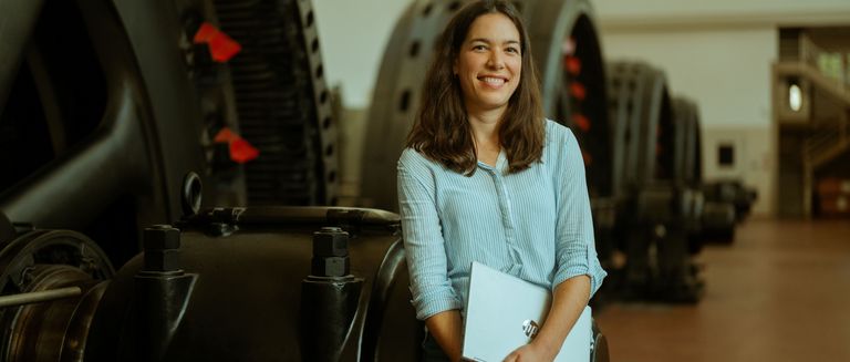 Freundliche Frau mit einem Klemmbrett, welche in einem Wasserkraftwerk steht